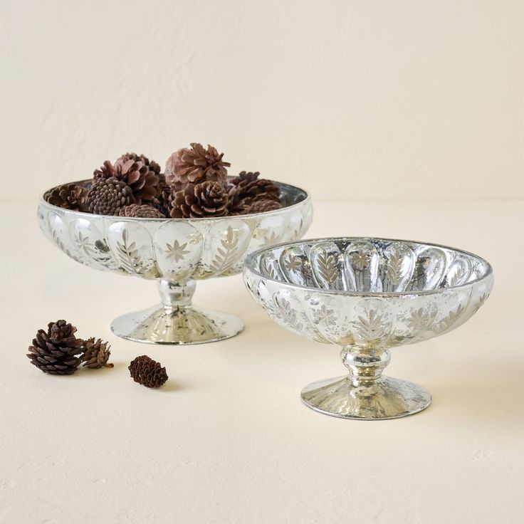 two silver bowls filled with pine cones on top of a table