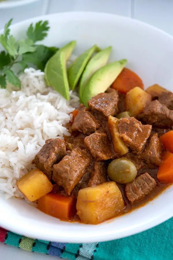 a white bowl filled with rice and meat next to an avocado on top