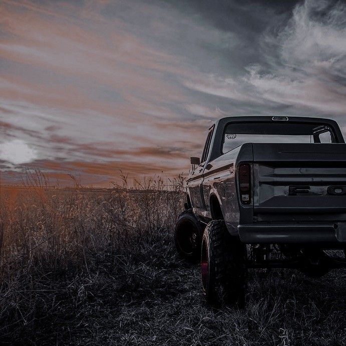 a truck parked in the middle of a field at sunset with clouds and grass behind it