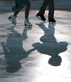 two people skating on an ice rink with shadows from the skateboarder's feet