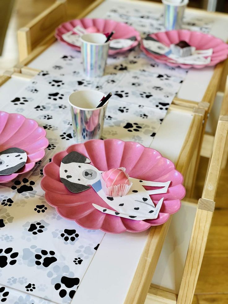 the table is set with pink plates and cups for dogs themed birthday party guests to eat