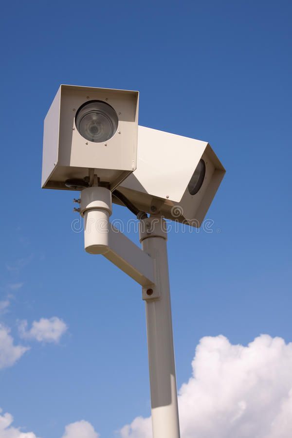 a white security camera on top of a pole with blue sky and clouds in the background