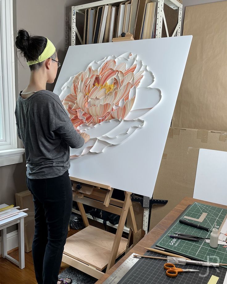 a woman standing in front of an easel with a large paper flower on it