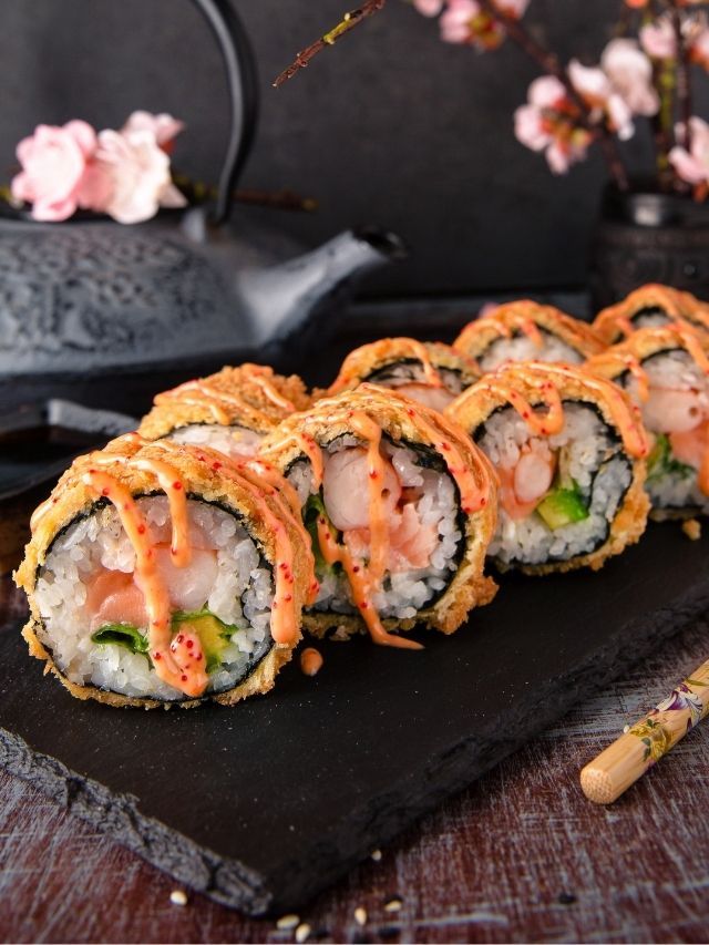 sushi rolls on a black plate with flowers in the background