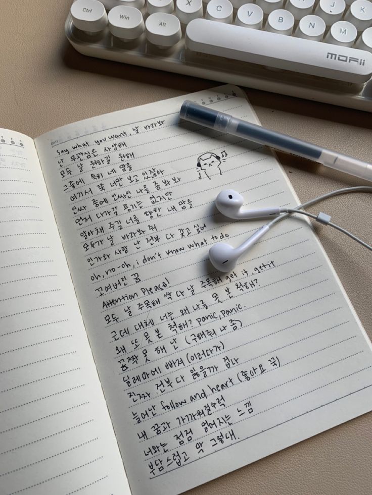 an open notebook with earbuds sitting on top of it next to a keyboard