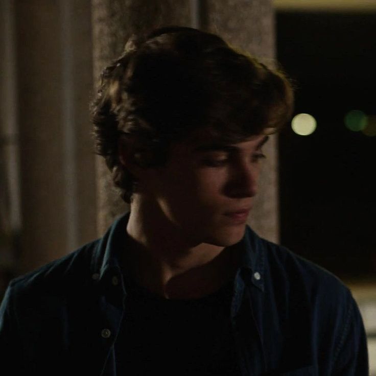 a young man standing in front of a building at night looking off into the distance