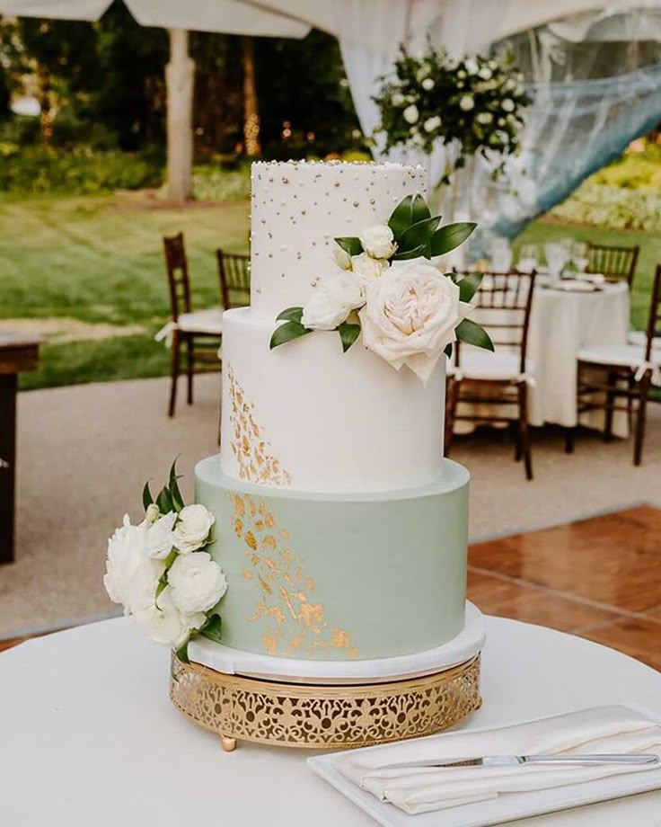 a three tiered cake with white flowers and gold trimmings on a table