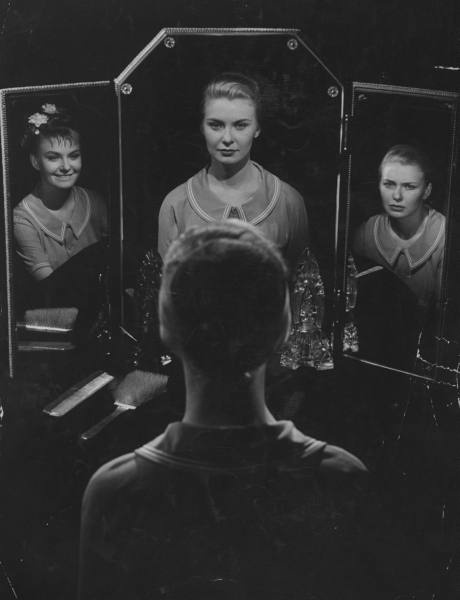 a woman standing in front of a mirror with three mirrors behind her and the reflection of another person's face