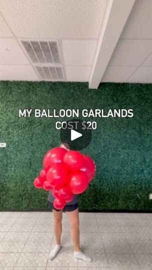 a person standing in front of a green wall holding red balloons with the words my balloon garlands cost $ 20