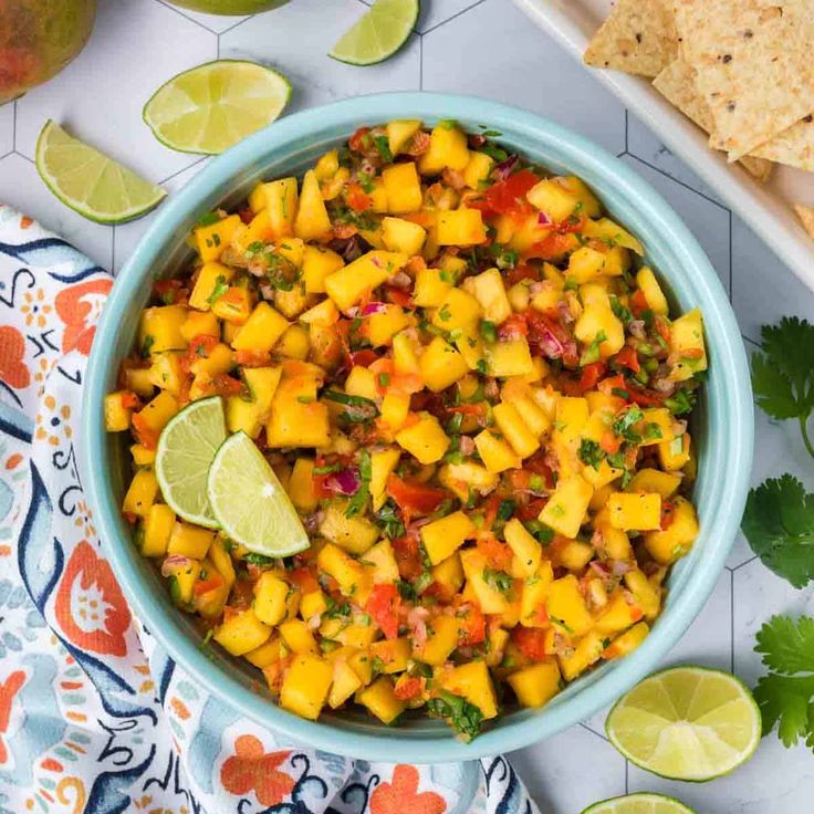 a blue bowl filled with mango salsa next to tortilla chips and lime wedges