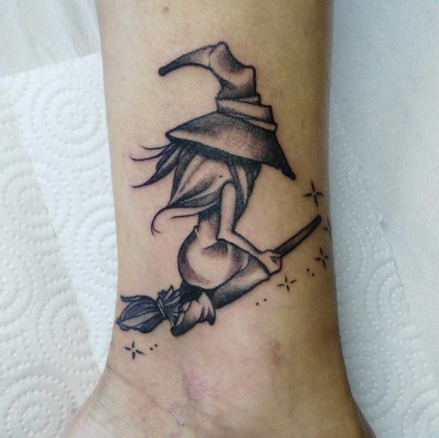 a woman's foot with a wizard hat and broom tattoo on her left ankle