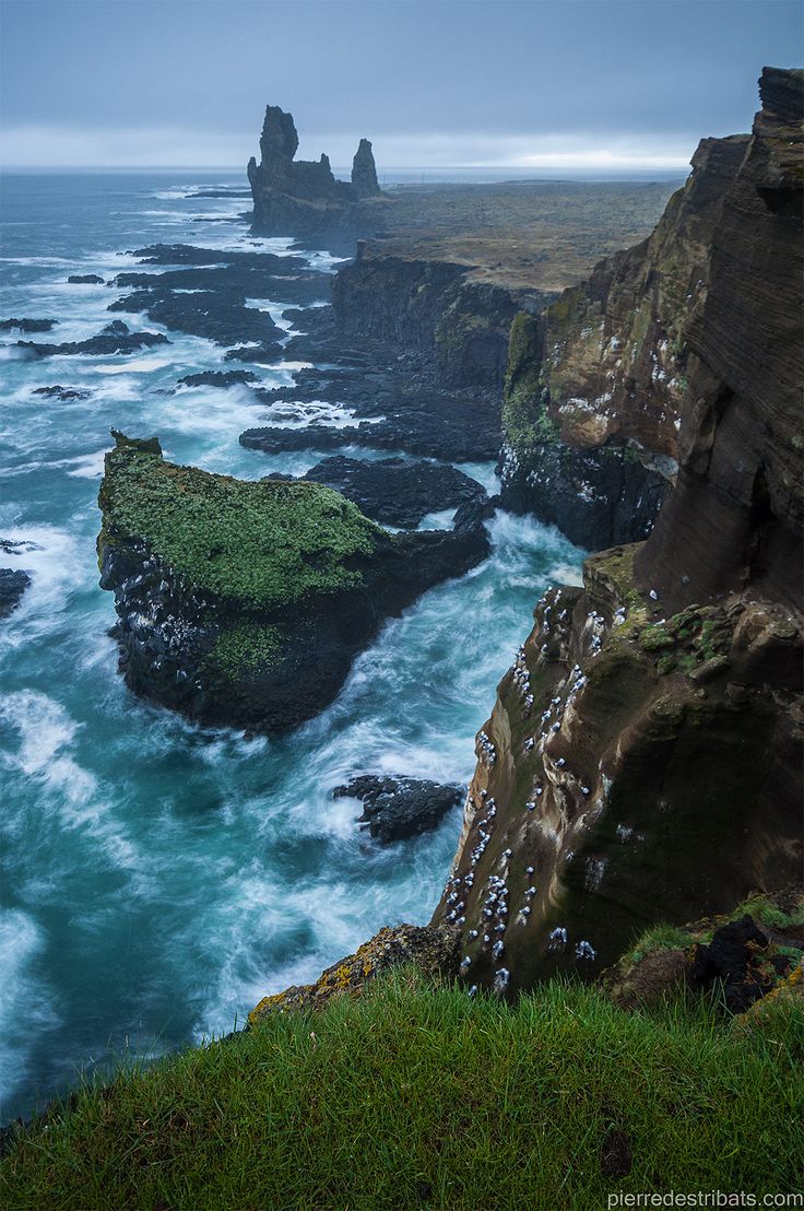 the ocean and cliffs are covered in green mossy vegetation, with dark clouds overhead