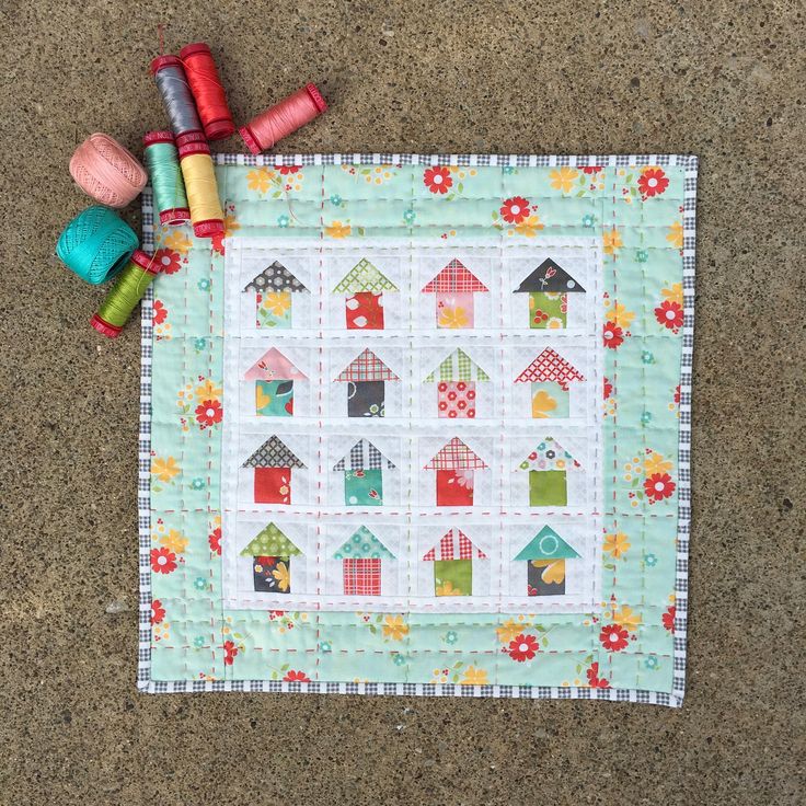 a quilted placemat with colorful houses and spools of thread on it