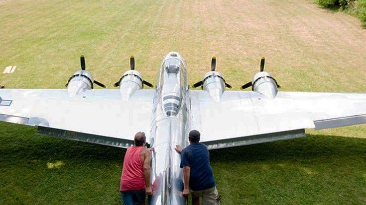 two people standing next to an airplane in the grass