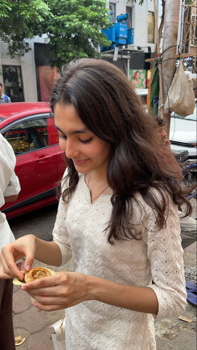 a woman is eating food on the street next to a red car and another man