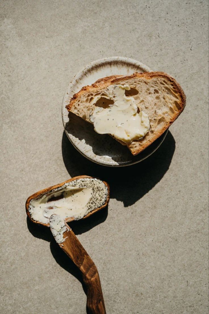 a piece of bread sitting on top of a white plate next to a bowl filled with butter