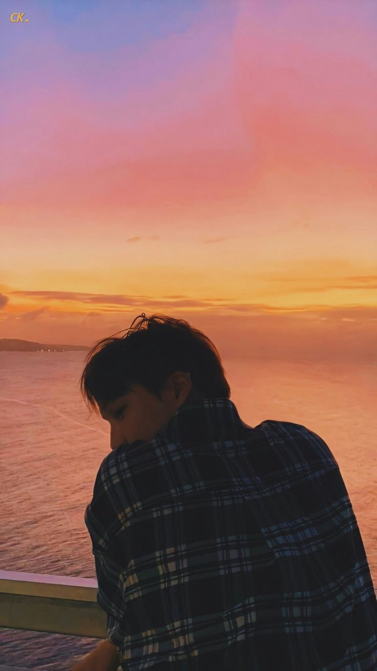 a person sitting on a bench looking at their cell phone while the sun is setting