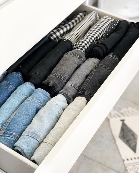 an open drawer filled with jeans on top of a tiled floor next to a rug