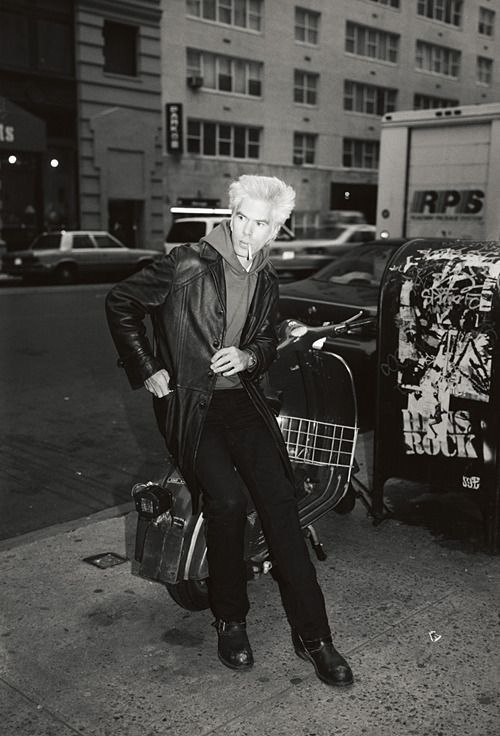 black and white photograph of an old woman sitting on a luggage bag in the street