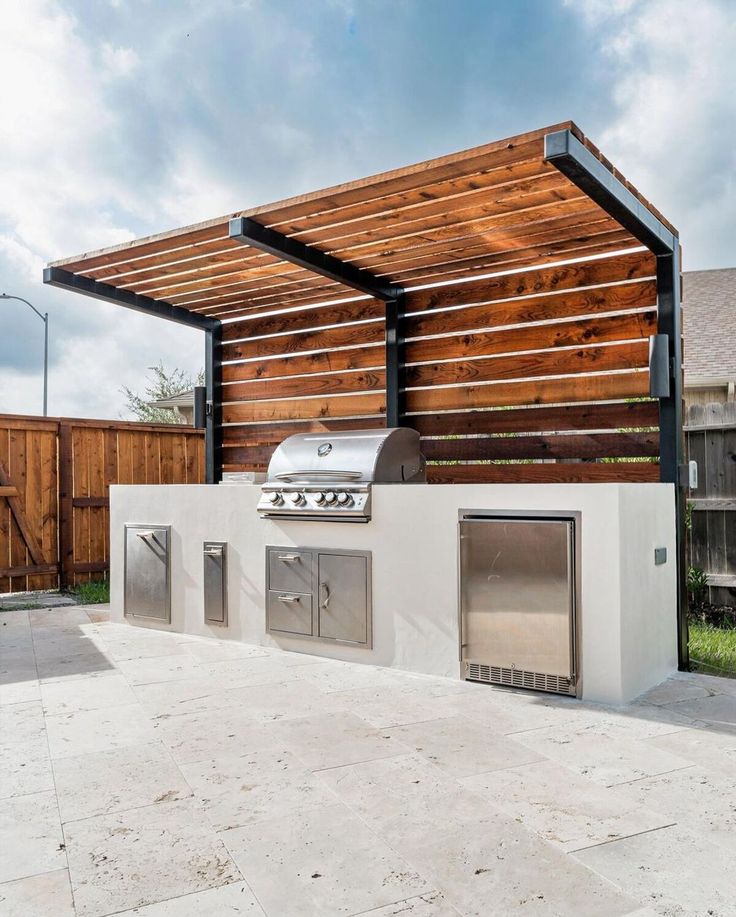 an outdoor bbq with grills and cabinets under a pergolated roof