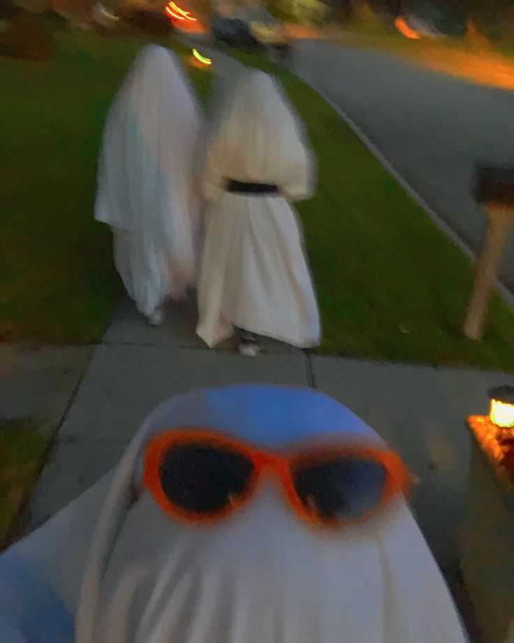 three people in white robes and sunglasses walking down a sidewalk with fire on the ground