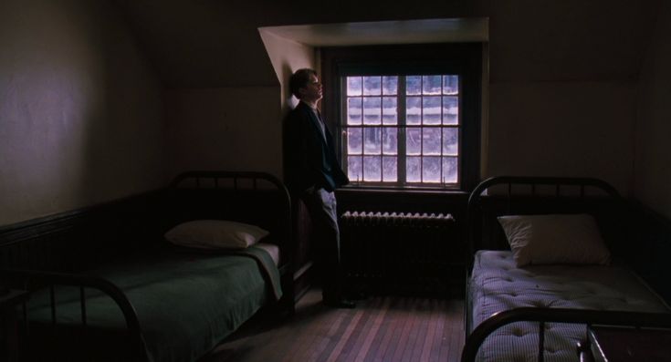 a man standing in front of a window next to two beds