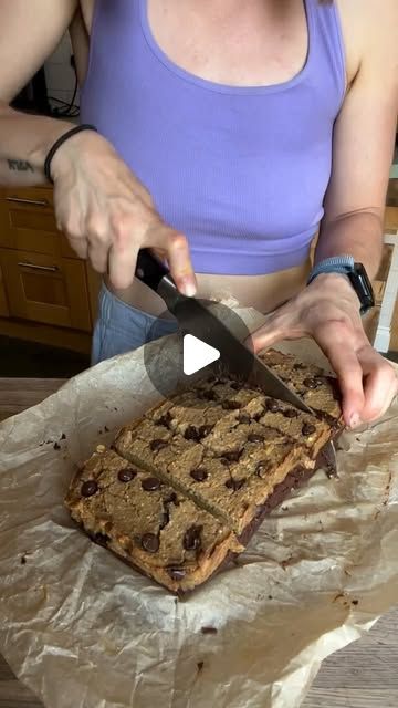 a woman cutting into a chocolate chip cookie bar with a pair of scissors on top of it