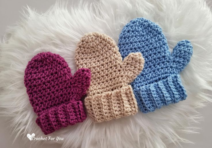 three crocheted mittens laying next to each other on a fluffy white surface