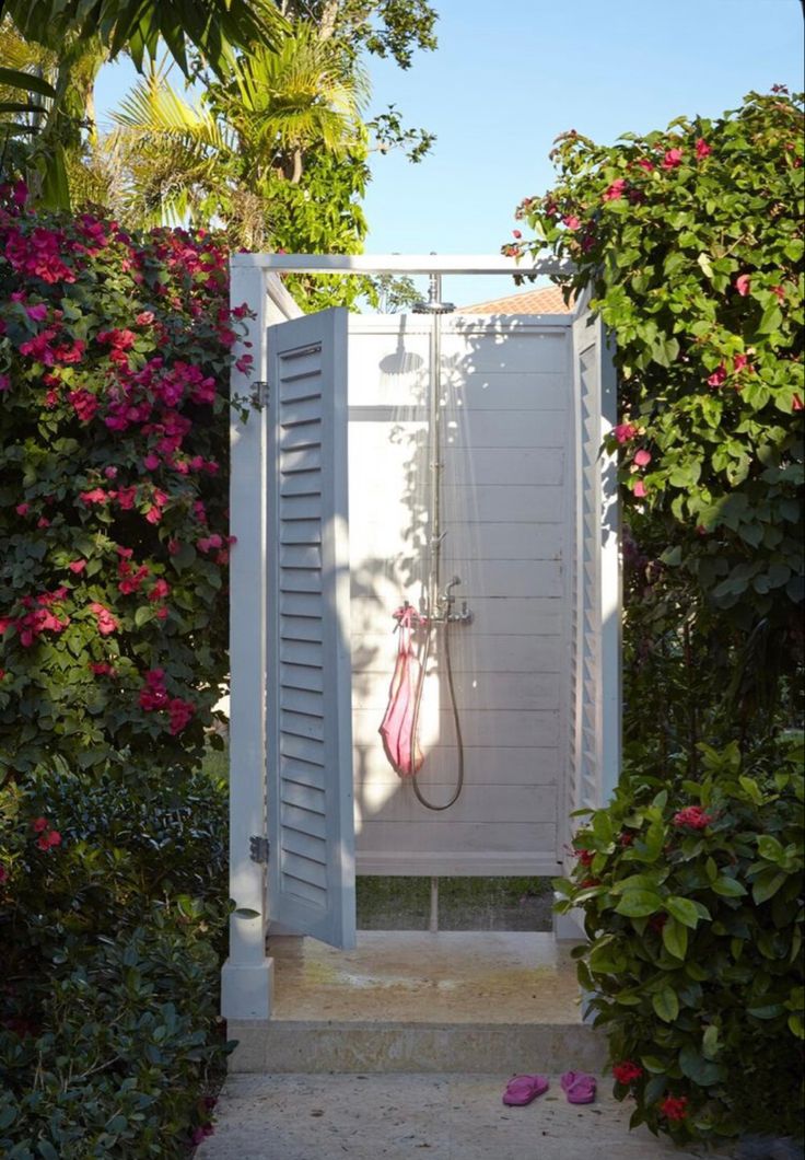 an open white door leading into a lush green garden with pink flowers on either side