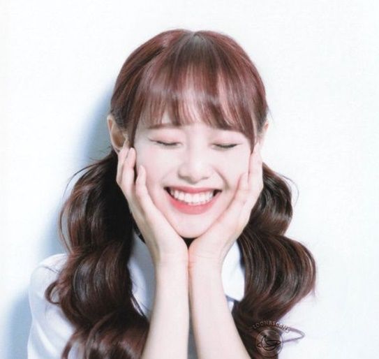 a woman with long hair smiling and holding her hands to her face while wearing a white shirt