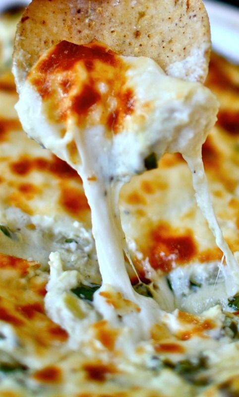 a hand dipping a tortilla chip into a white bowl filled with spinach dip