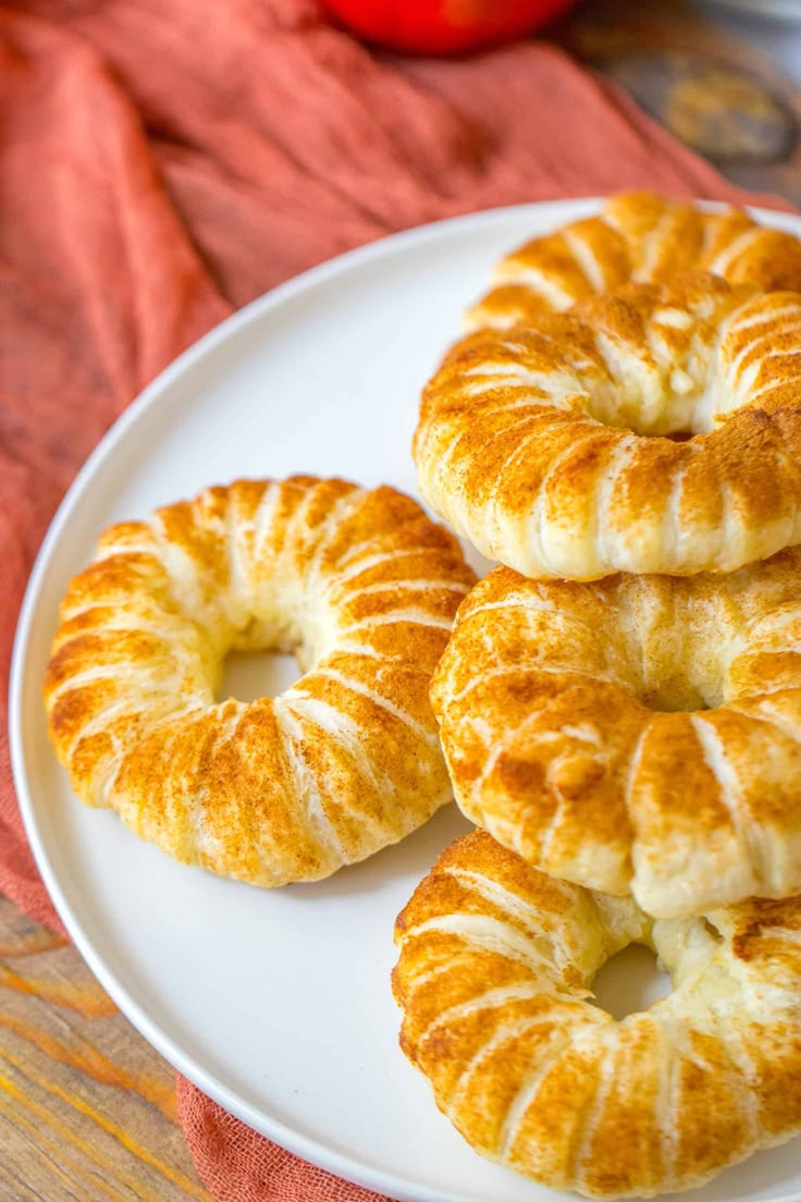 four croissants on a white plate with an apple in the background