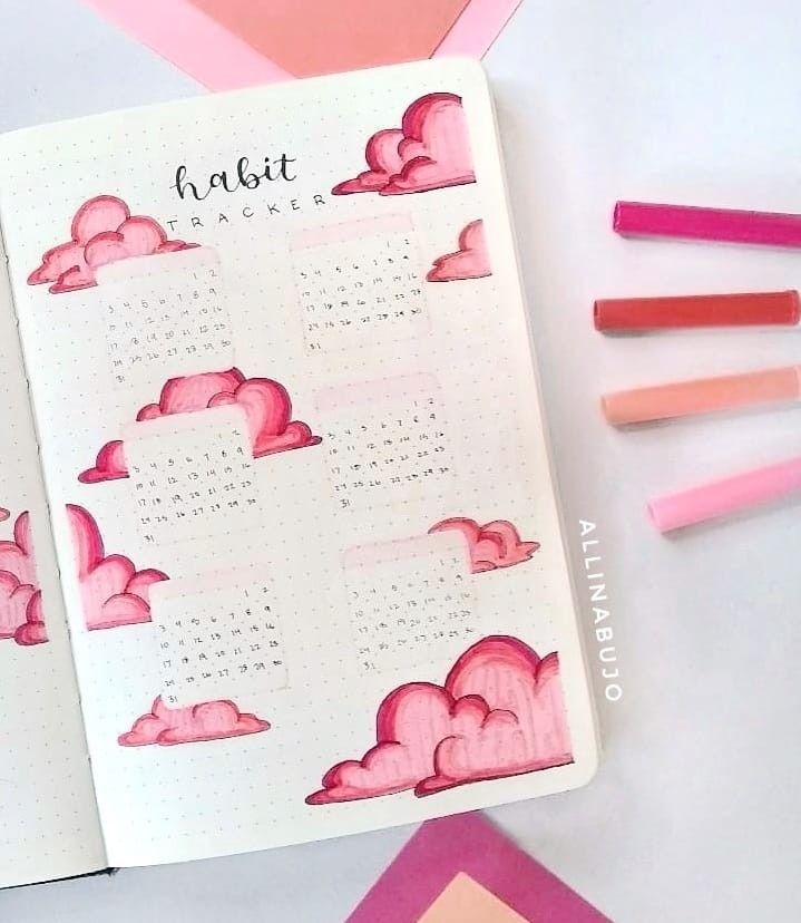 an open planner with pink clouds and pencils next to it on a white surface