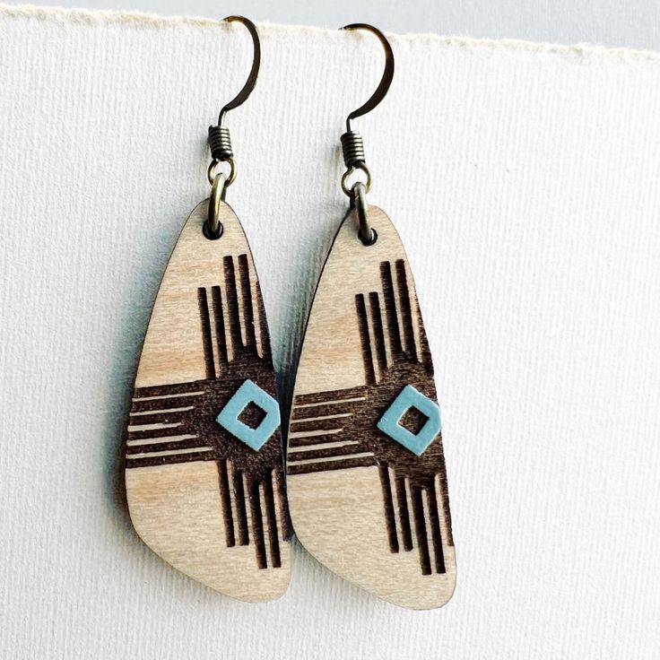 wooden earrings with blue and brown designs hanging from hooks on a white surface next to a piece of fabric