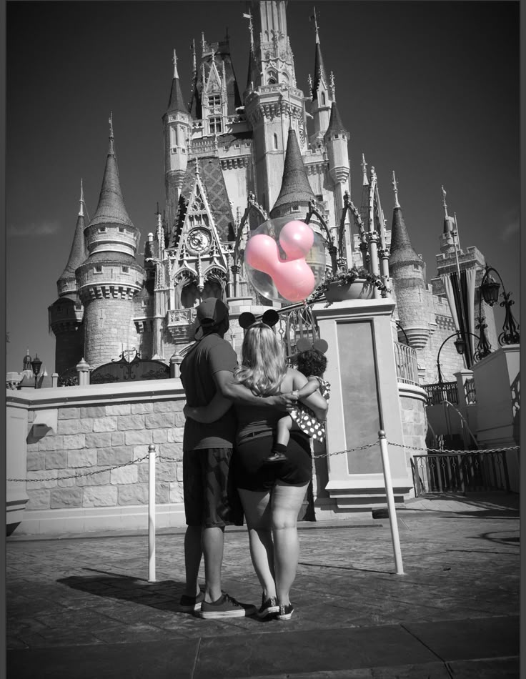 three people standing in front of a castle with a pink heart shaped balloon attached to it