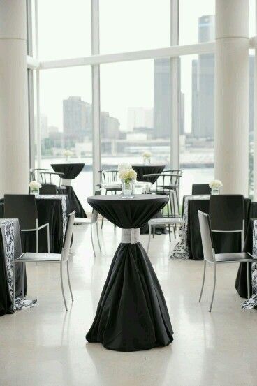 tables and chairs with black tablecloths are set up in front of large windows