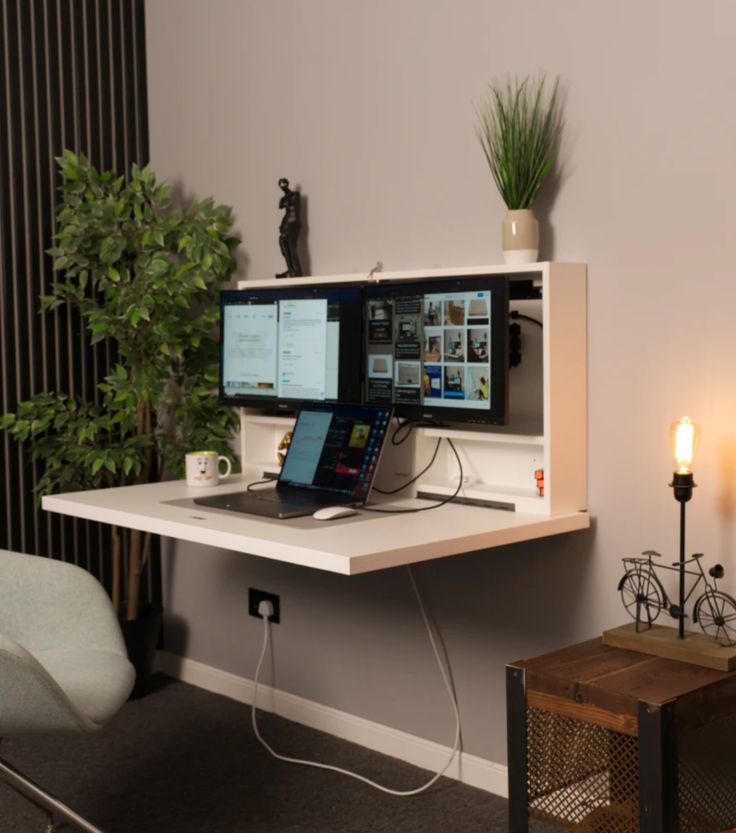 a computer desk with two monitors and a laptop on it in front of a plant