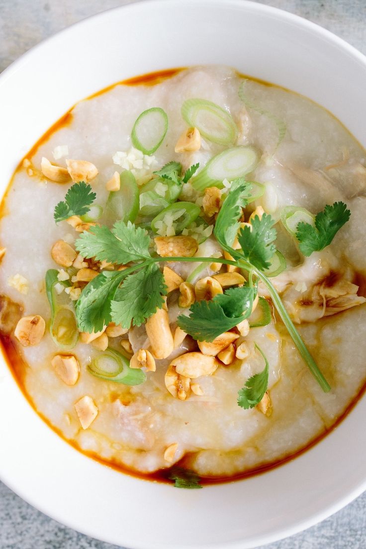 a white bowl filled with soup and garnished with cilantro, peanuts, and green onions