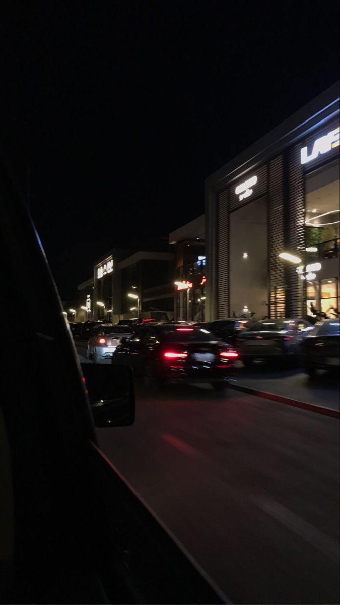 cars are driving down the street at night in front of a building with lit up windows