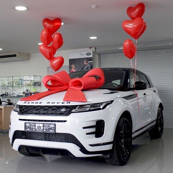 a white range rover with red heart balloons tied to it's hood in a showroom