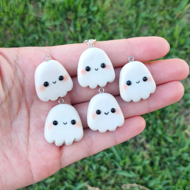 four white ghost charms with black eyes are held in someone's hand