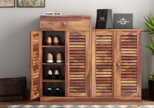 a wooden cabinet with two doors and shoes on it next to a potted plant