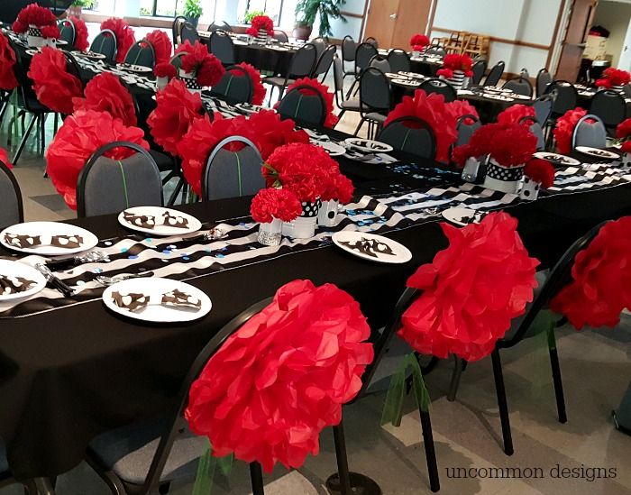 the tables are set up with black and white plates, silverware, and red carnations