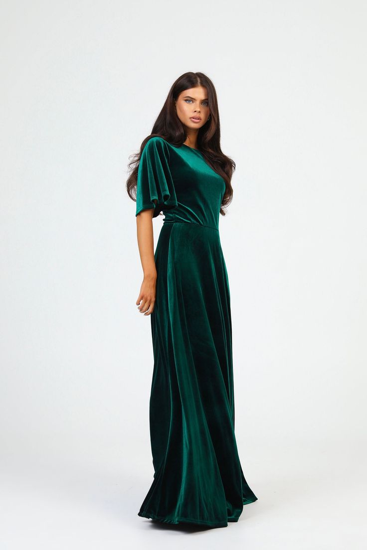 a woman in a green velvet dress standing on a white background with her hands behind her back