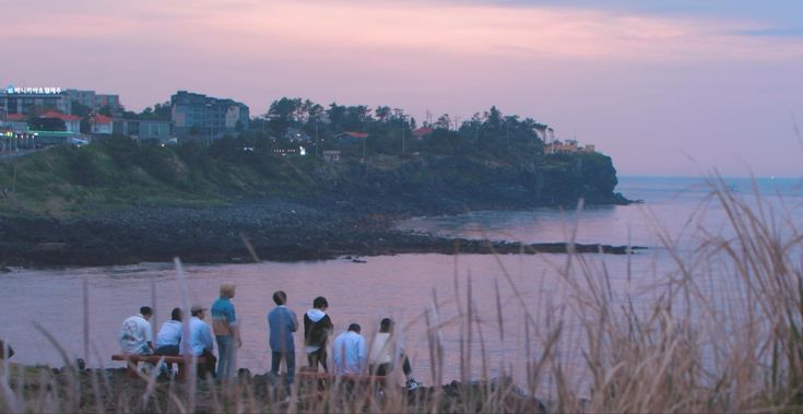 a group of people standing on top of a beach next to the ocean at sunset