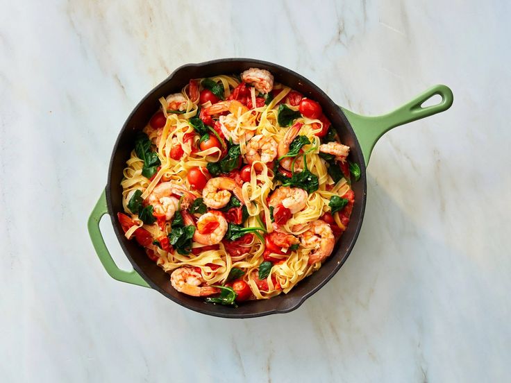 a pan filled with pasta and shrimp on top of a marble countertop next to a green spatula