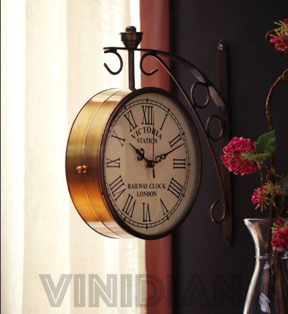 a clock hanging from the side of a wall next to a vase with flowers in it