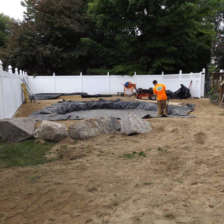 a man in an orange shirt standing next to a white fence and some large rocks