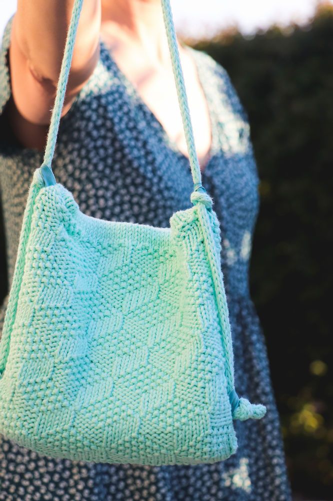 a woman is holding a crocheted bag in her hand