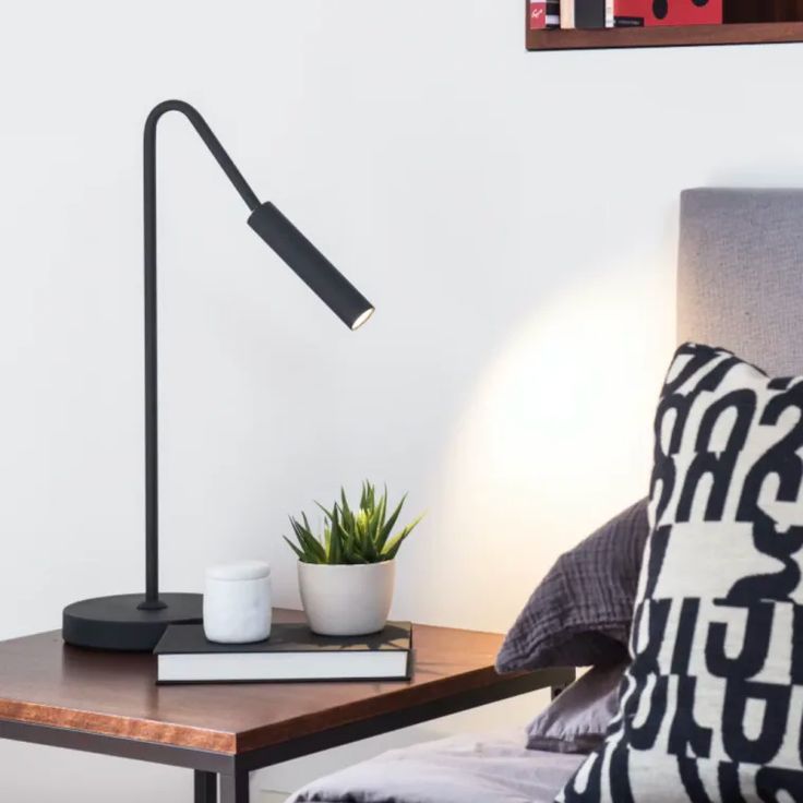 a table with a lamp on it next to a book and a potted plant